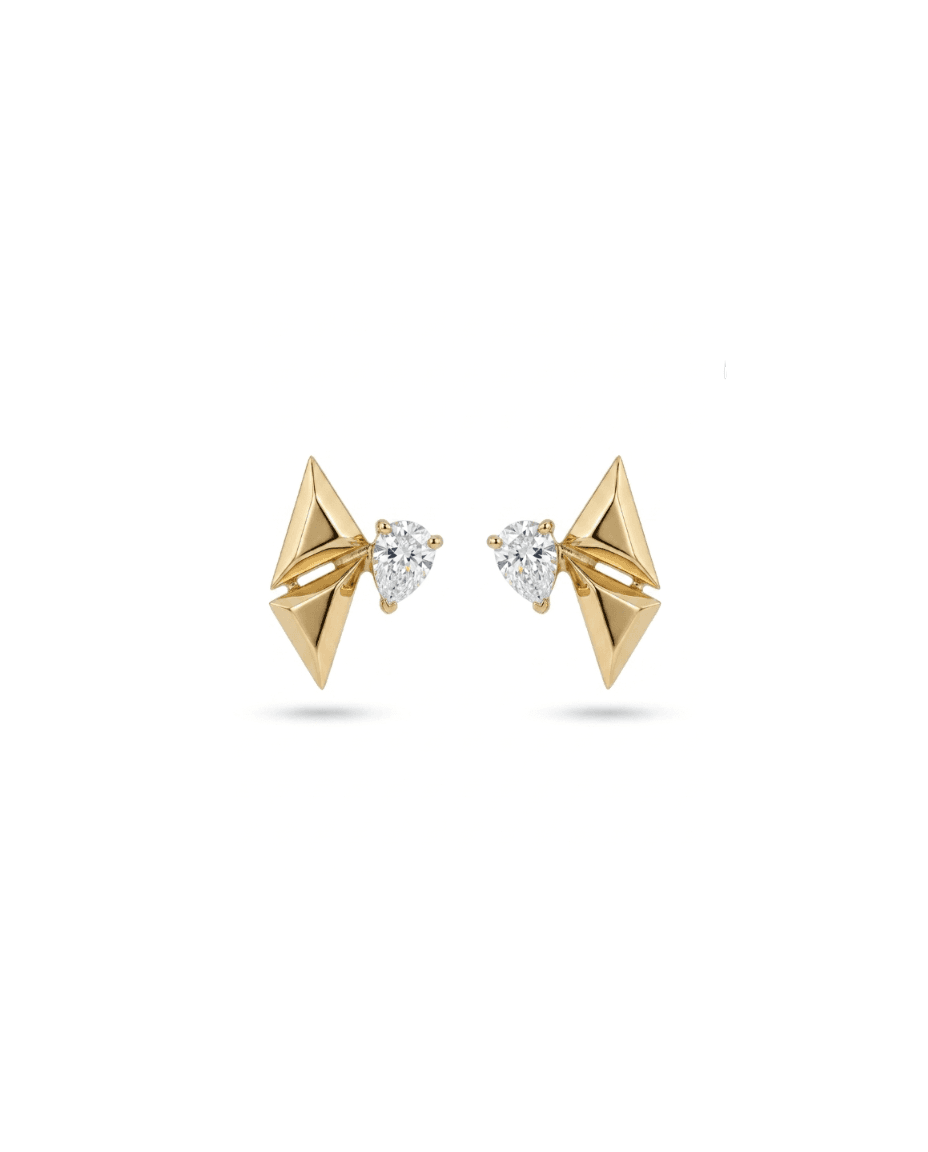 A pair of gold geometric stud earrings with triangular pyramid shapes and a small pear-cut clear gemstone in the center, set against a plain white background.